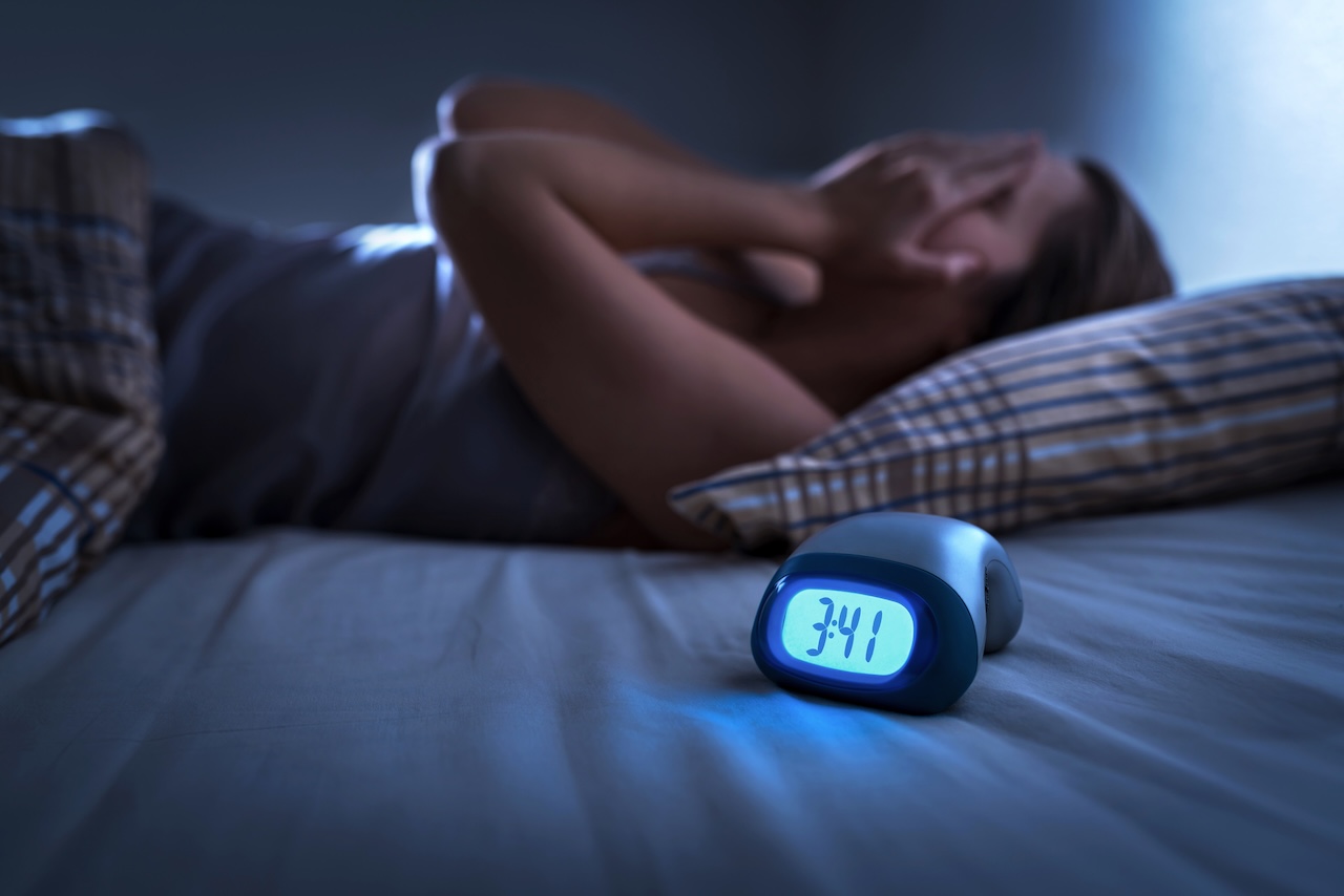 Woman awake in bed with clock showing 3:41