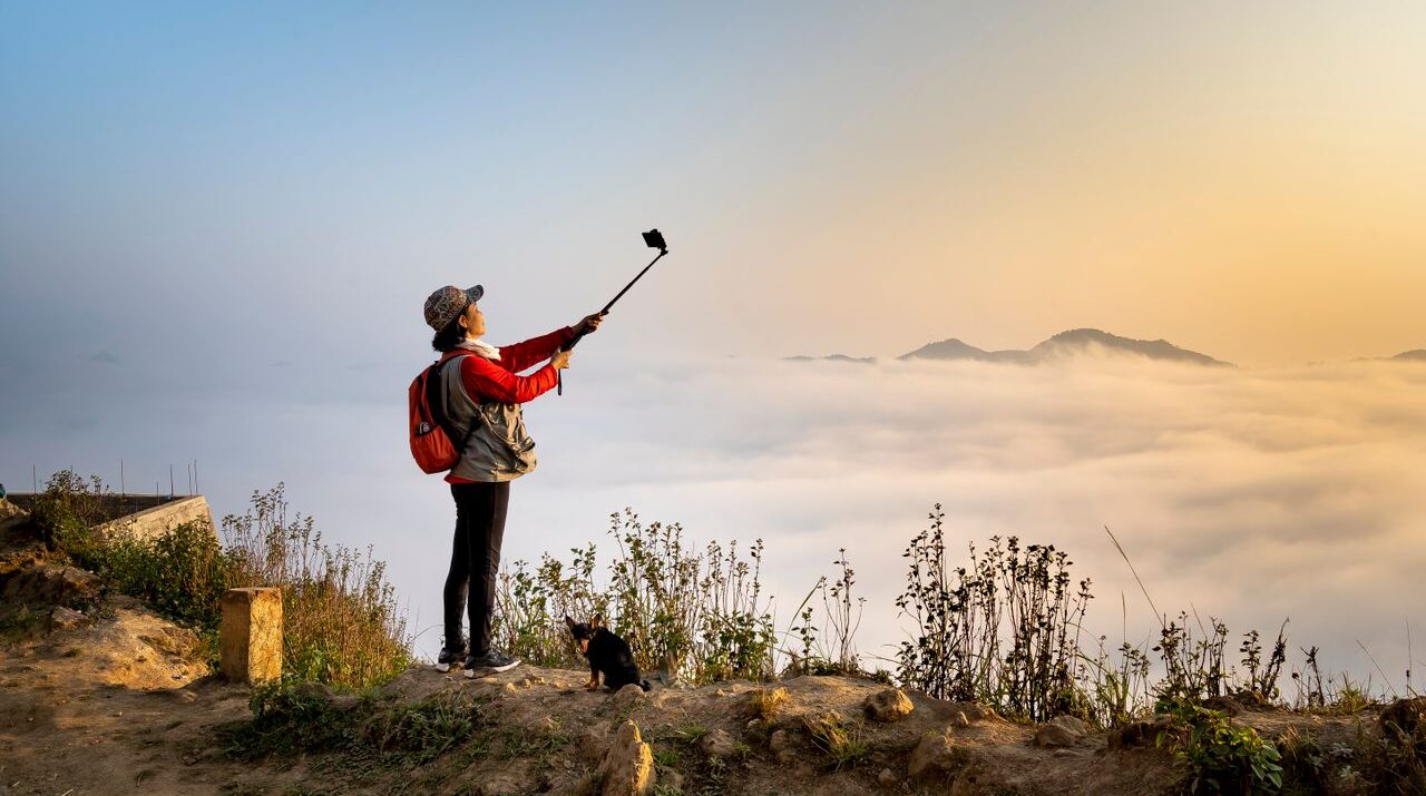 a woman works on creating lore using a selfie stick and recording content while in the beauty of nature